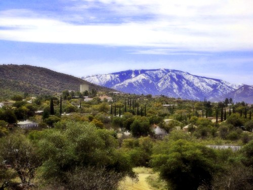 A scenic view of a mountainous landscape with snow-capped peaks, lush greenery, and a small town in the foreground.