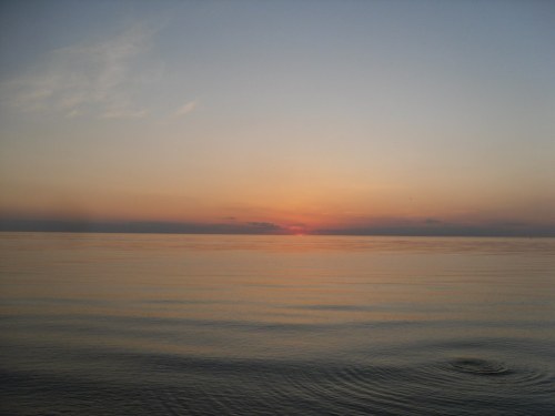 A serene sunset over calm waters, with soft hues of orange and blue reflecting on the surface.