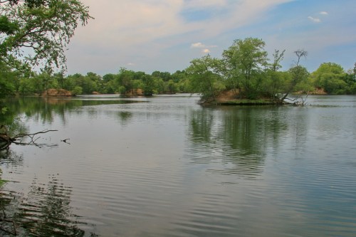 A serene lake surrounded by lush greenery and small islands under a partly cloudy sky.