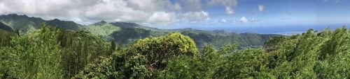 A panoramic view of lush green mountains and a distant ocean under a partly cloudy sky.