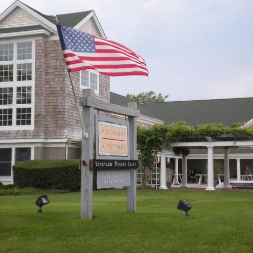 Sign for Pellegrini Vineyards with an American flag in front of a large building and green lawn.