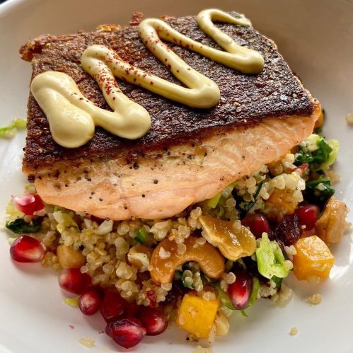 A beautifully plated dish featuring seared salmon on a bed of quinoa salad with pomegranate and a drizzle of sauce.