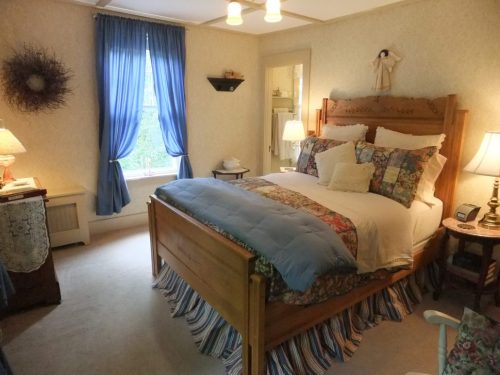 Cozy bedroom with a wooden bed, floral bedding, blue curtains, and warm lighting from bedside lamps.