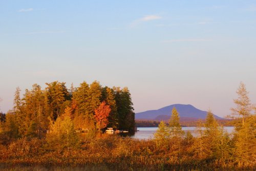 A serene lake scene with colorful autumn trees and a distant mountain under a clear sky.