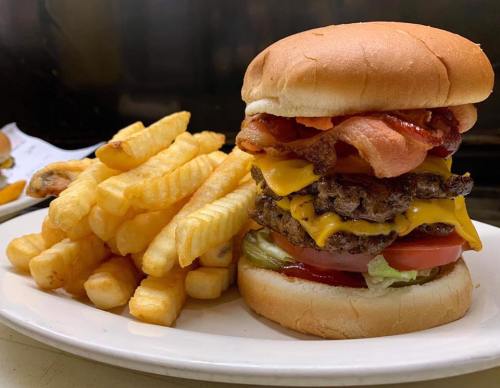 A towering cheeseburger with bacon, lettuce, and tomato, served with a side of golden French fries.