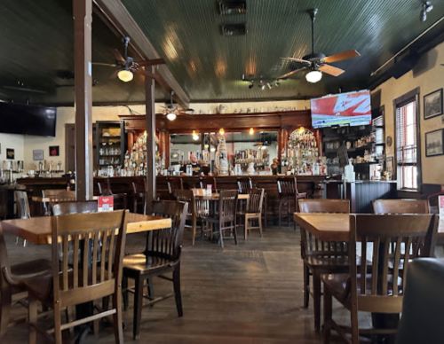 Interior of a restaurant with wooden tables, chairs, a bar, and a TV displaying a sports game.