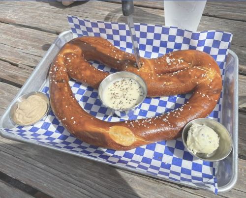 A large, soft pretzel on a tray with dipping sauces, including mustard and cheese, on a checkered paper background.