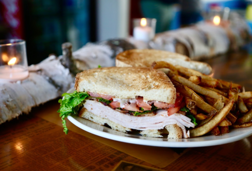 A plate with a turkey sandwich layered with lettuce, tomato, and fries, set on a rustic wooden table.