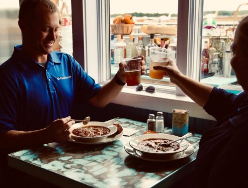 Two people at a table enjoying meals and drinks, smiling and toasting with their glasses.