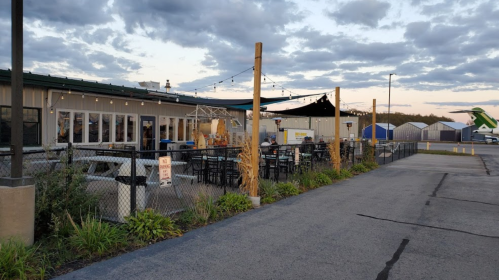 A restaurant with outdoor seating, string lights, and a view of storage units under a cloudy sky.