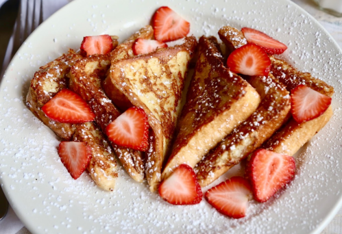 A plate of French toast slices topped with fresh strawberries and powdered sugar.