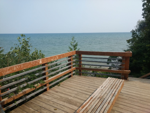 A wooden deck overlooking a calm lake with trees on the shore and a clear sky in the background.
