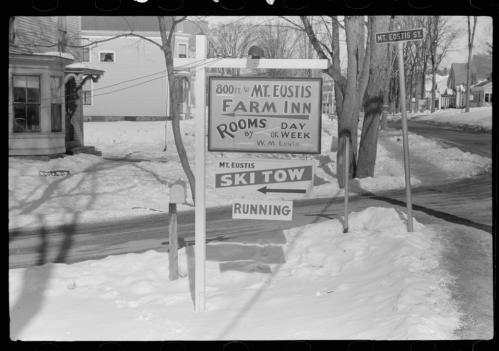 Sign for Mt. Eustis Farm Inn with directions for rooms, ski tow, and street name, surrounded by snow.