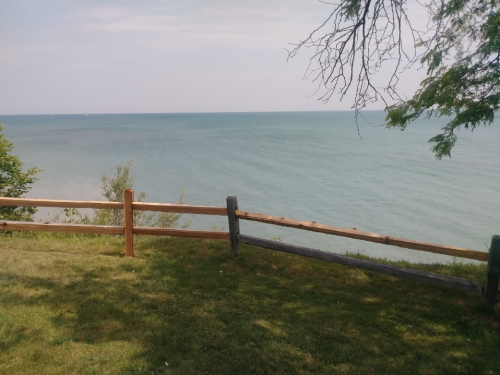 A serene view of a lake with a wooden fence and grassy area under a clear sky.
