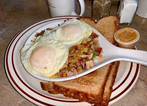 A plate with two sunny-side-up eggs on a bed of hash browns, served with toast and a side of sauce.