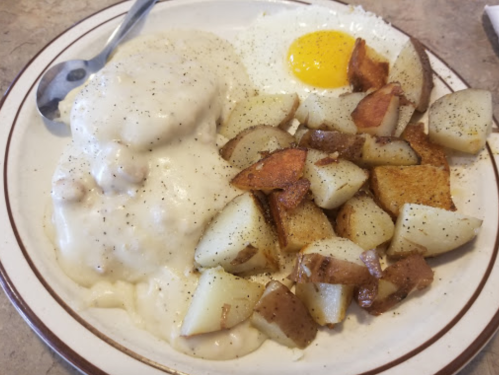 A plate of breakfast featuring biscuits and gravy, a sunny-side-up egg, and seasoned roasted potatoes.