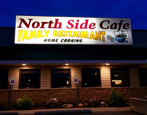 Sign for North Side Cafe, a family restaurant, featuring "Home Cooking" in bright colors, illuminated at dusk.