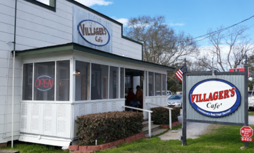 Exterior of Villager's Cafe with a sign reading "OPEN" and an American flag, surrounded by greenery and blue sky.