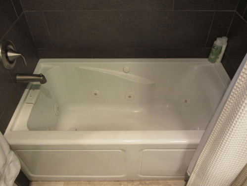 A clean, white bathtub with jets, set against dark tiled walls and a shower curtain.