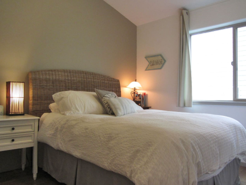 Cozy bedroom with a large bed, bedside lamp, and window, featuring neutral tones and soft bedding.