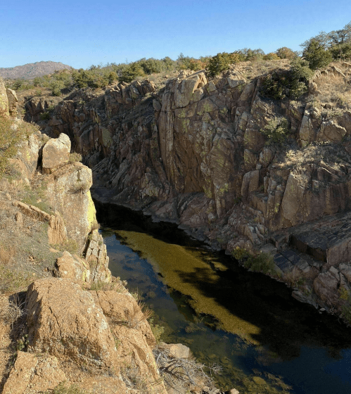 A rocky canyon with steep walls and a narrow river running through it, surrounded by sparse vegetation and clear blue skies.