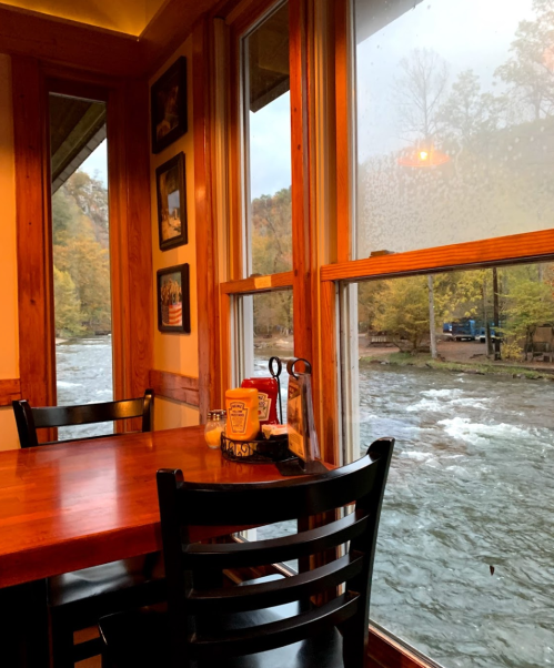 A cozy restaurant table by a window overlooking a river and autumn trees, with condiments on the table.