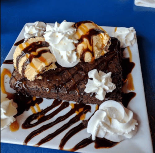 A rich chocolate brownie topped with two scoops of ice cream, drizzled with chocolate sauce and surrounded by whipped cream.