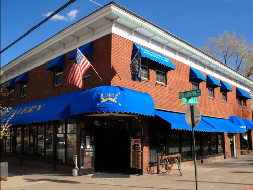 A brick building with blue awnings, flags, and a sign for California Street, featuring a bicycle parked outside.