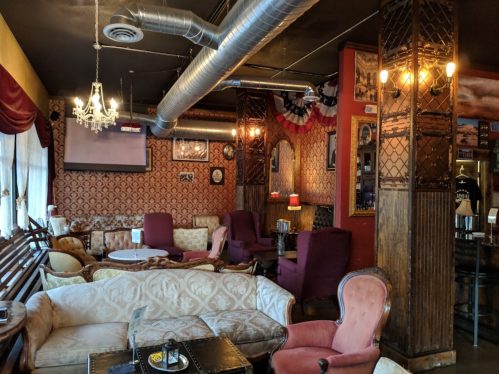 Cozy café interior with vintage decor, plush seating, and warm lighting, featuring patterned wallpaper and a chandelier.
