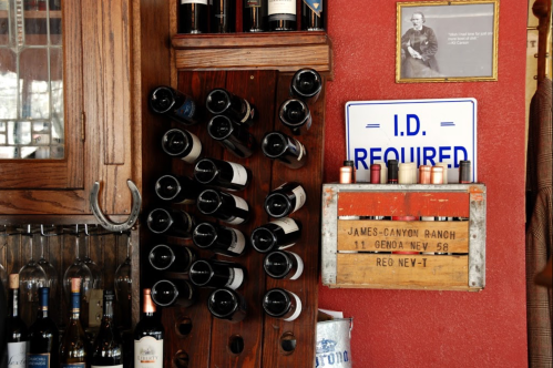 A rustic bar scene featuring a wine rack, bottles, and a sign that reads "I.D. REQUIRED."