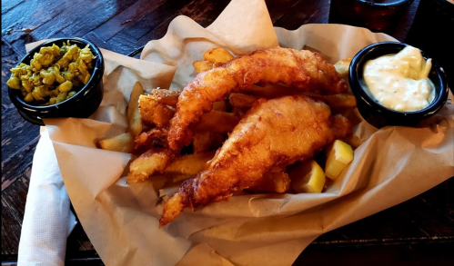 A plate of golden-battered fish and chips, served with tartar sauce and a side of green peas.