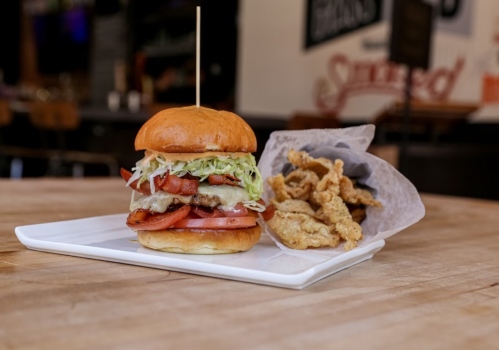 A delicious burger with lettuce, tomato, and a skewer, served with a side of crispy fried chicken on a plate.