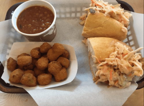 A tray with two sandwiches filled with coleslaw, a cup of baked beans, and a serving of fried okra.
