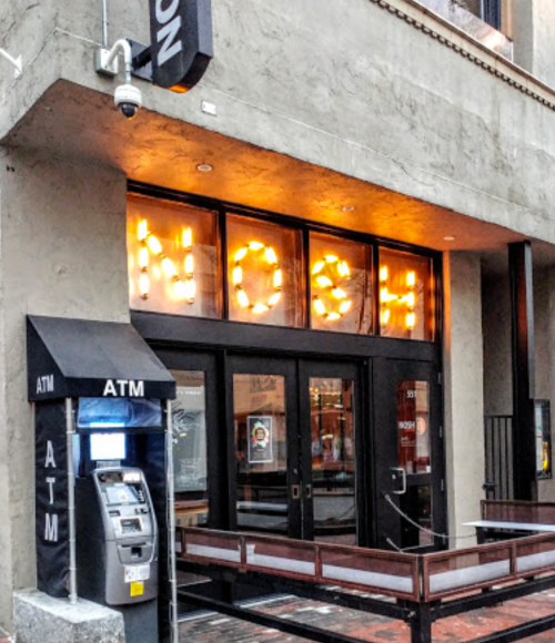 Exterior of a building with illuminated windows spelling "NOAH" and an ATM nearby.