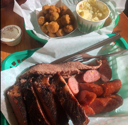 A plate of barbecue featuring brisket, sausage, and sides of fried okra and potato salad in green baskets.