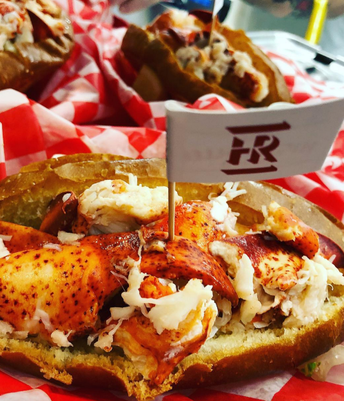 A close-up of a lobster roll in a toasted bun, topped with lobster meat and a small flag with "FR" on it.