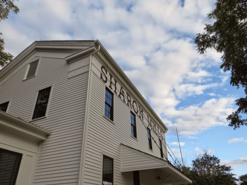 A white building with "SHARON" painted on the side, under a partly cloudy blue sky.