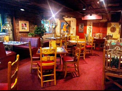 Cozy restaurant interior with colorful decor, wooden chairs, and vibrant artwork on the walls. Warm, inviting atmosphere.