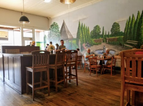 A cozy restaurant interior with wooden furniture and a mural of a scenic landscape on the wall.
