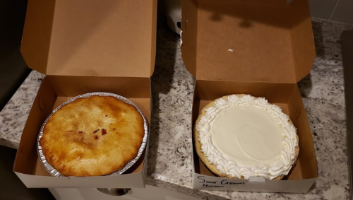 Two dessert boxes on a countertop: one with a baked pie and the other with a sour cream pie topped with white frosting.