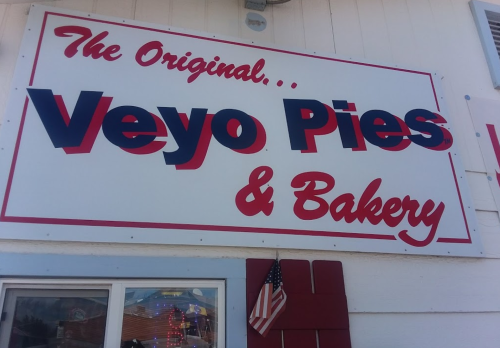 Sign for "The Original Veyo Pies & Bakery" with red and blue lettering, featuring an American flag below.