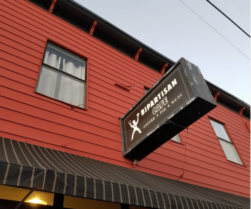 Sign for Bipartisan Cafe, featuring coffee, beer, and wine, on a red building with a striped awning.