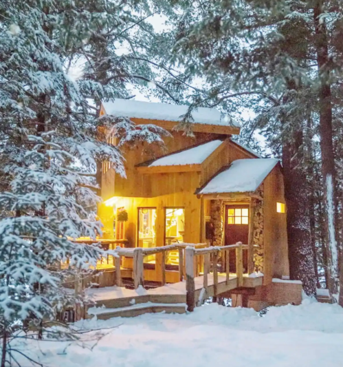 A cozy wooden cabin surrounded by snow-covered trees, warmly lit in a winter landscape.