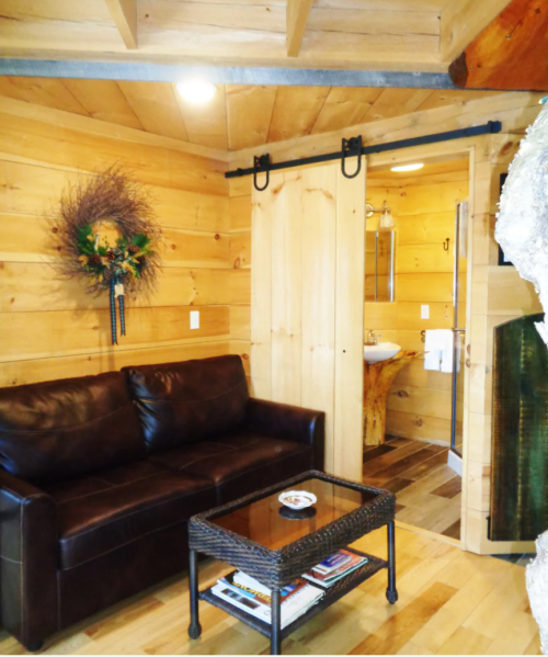 Cozy wooden interior featuring a leather sofa, a sliding barn door, and a small coffee table with magazines.