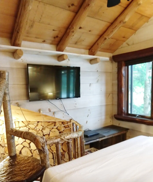 Cozy cabin interior featuring a wooden ceiling, a TV on the wall, and a view through a window.