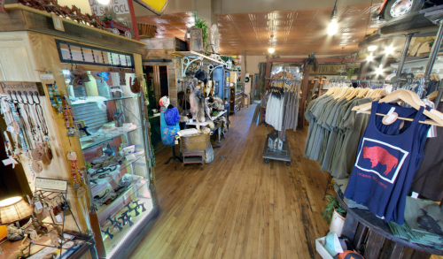 A cozy shop interior featuring wooden floors, display cases, clothing racks, and various rustic decor items.