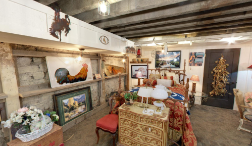 A cozy vintage room with rustic decor, featuring a wooden ceiling, antique furniture, and various artworks on the walls.