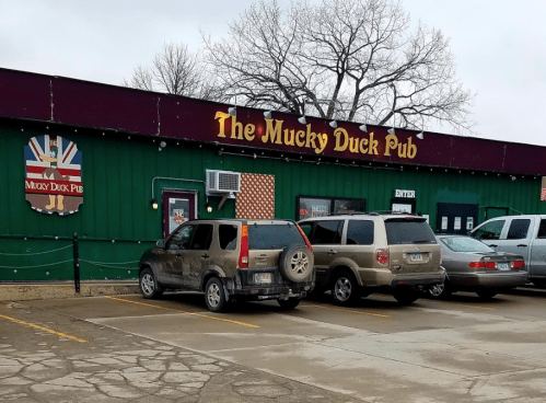 Exterior of The Mucky Duck Pub, featuring a green facade, parking lot, and cloudy sky.