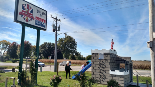 A playground slide next to a castle structure, with a sign for a restaurant in the background and clear blue skies.