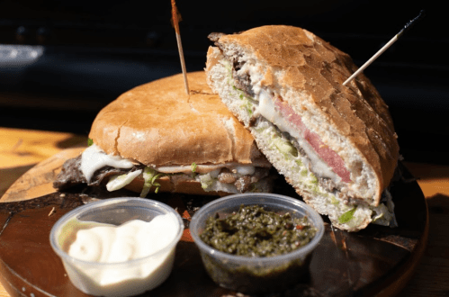 A hearty sandwich with layers of meat, cheese, and vegetables, served with sauces on the side.